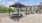 a patio with tables and chairs and a covered area with buildings in the background